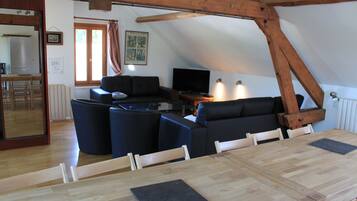 A cozy living room with a wooden dining table, a sofa, and a television.