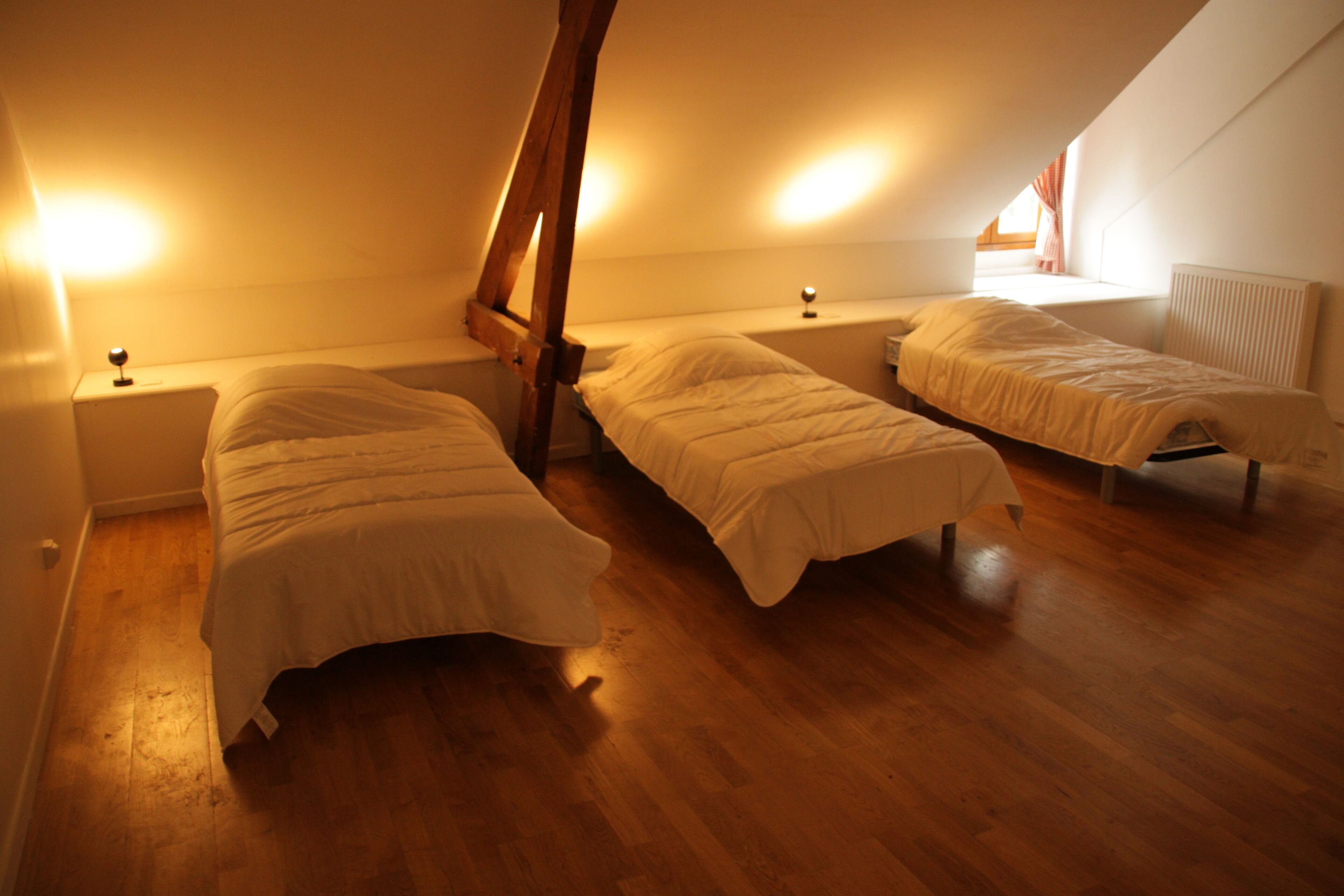A room with two beds, wooden flooring, and a sloped ceiling.