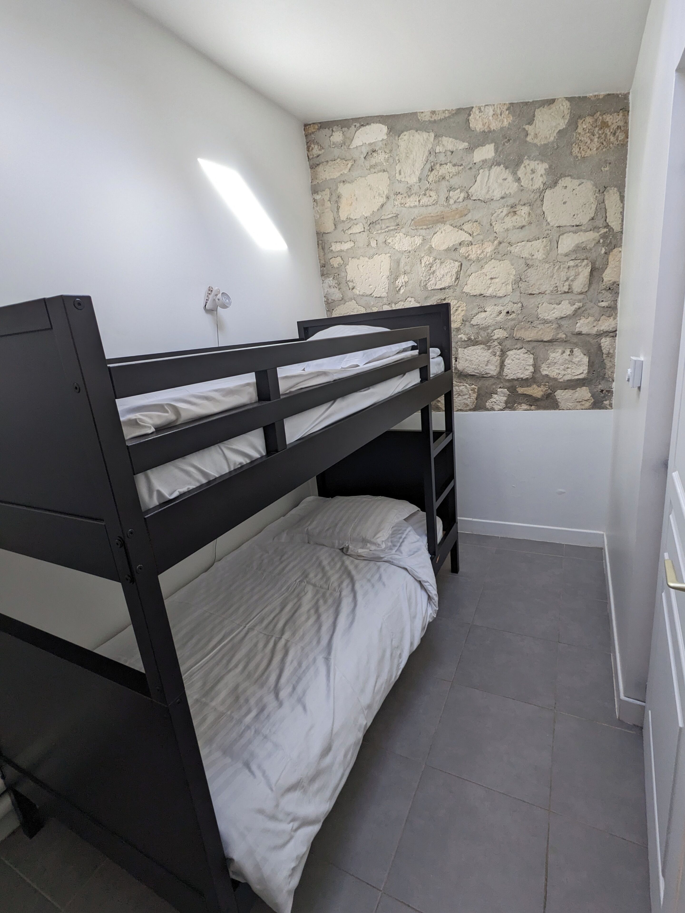 Een slaapkamer met een stapelbed, een stenen muur en een witte plafondlamp.