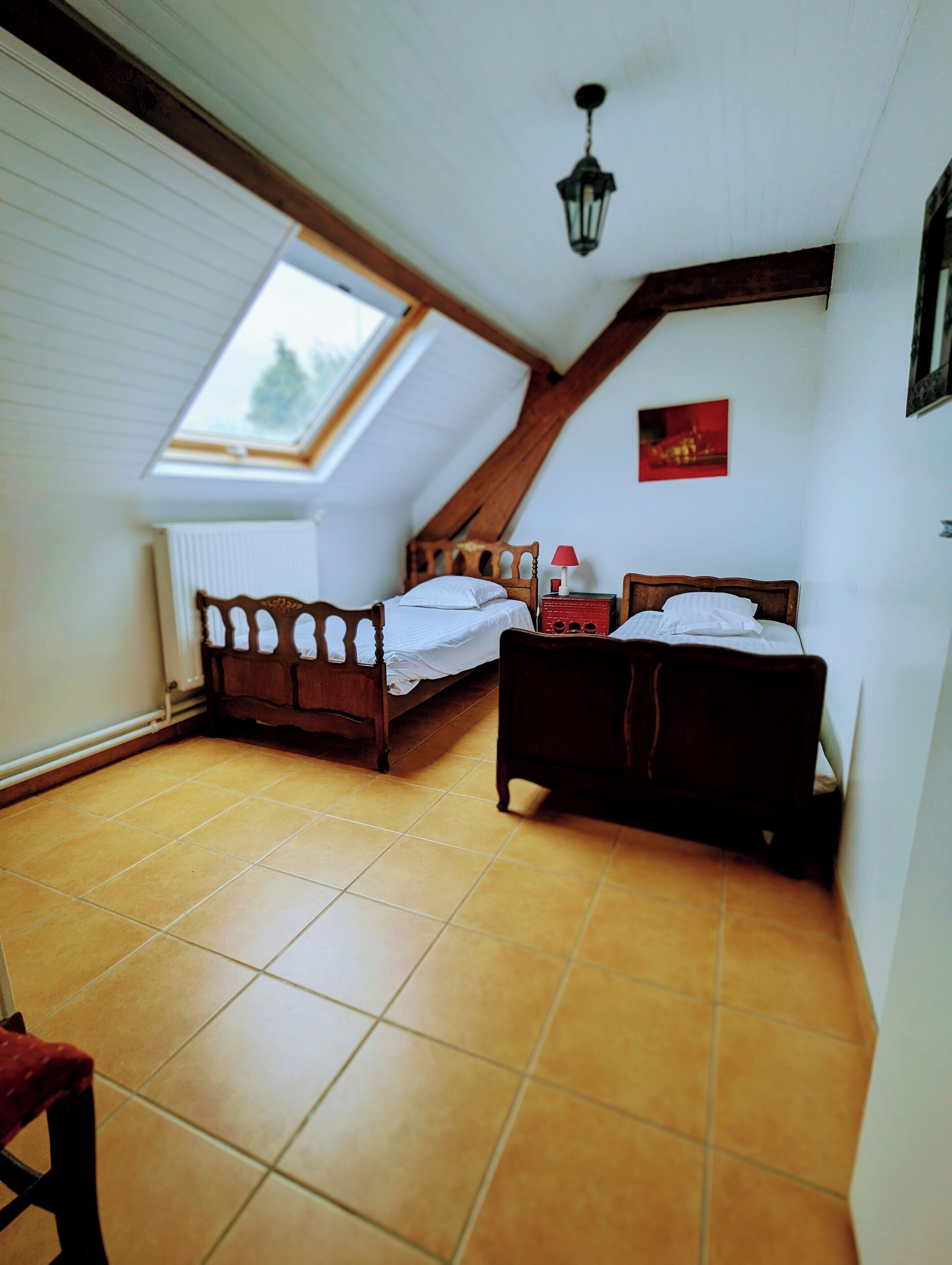 A bedroom with two beds, a skylight, a radiator, and a hanging light fixture.