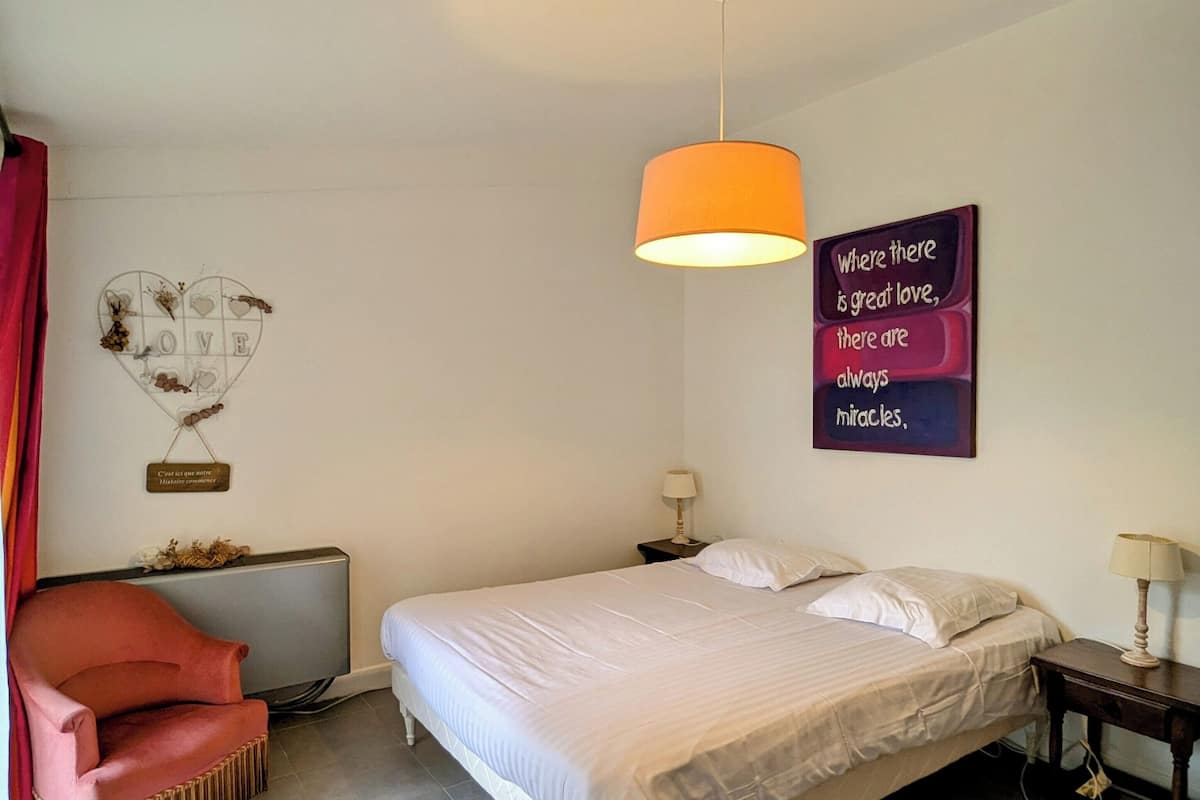 A bedroom with a bed, a chair, a wall-mounted lamp, and a motivational quote on the wall.
