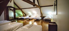 A dormitory-style room with multiple single beds arranged in rows, wooden beams on the ceiling, and a large mirror on one wall. - Le Translon  (Saint-Pierre-Aigle)
