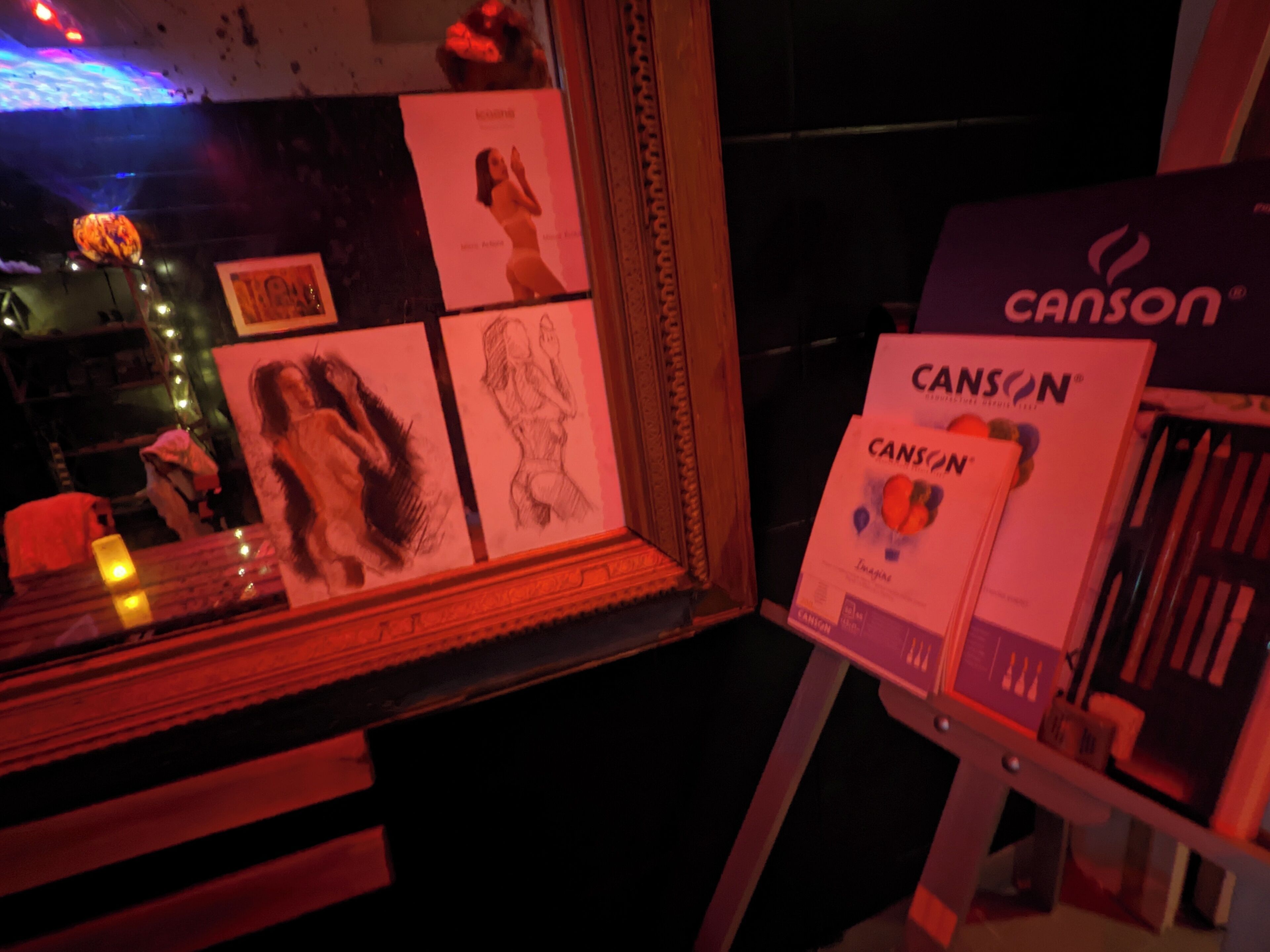 Presentación de cuadernos Canson y lápices en una habitación con poca luz y obras de arte en la pared.