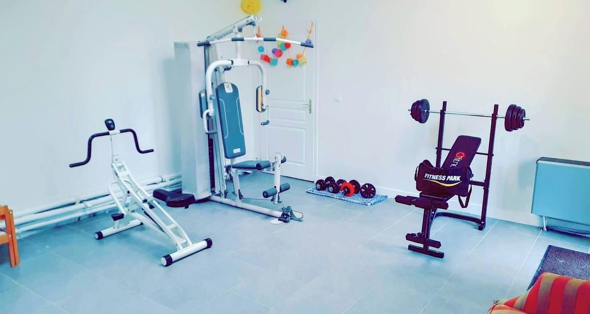 Un gimnasio con equipo de ejercicio, incluyendo una cinta de correr, banco de pesas y mancuernas.
