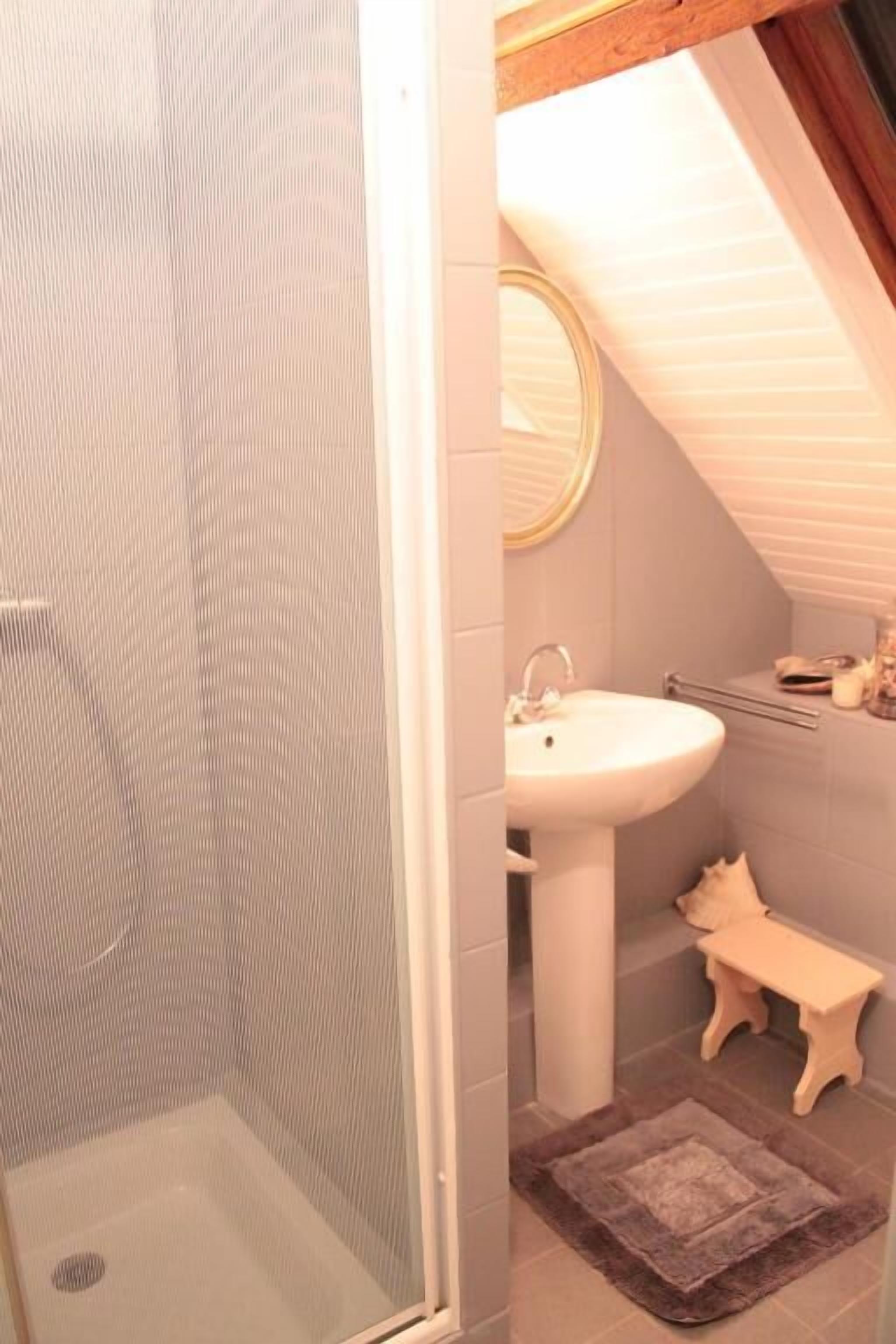 Baño con ducha, lavamanos y un pequeño banco.