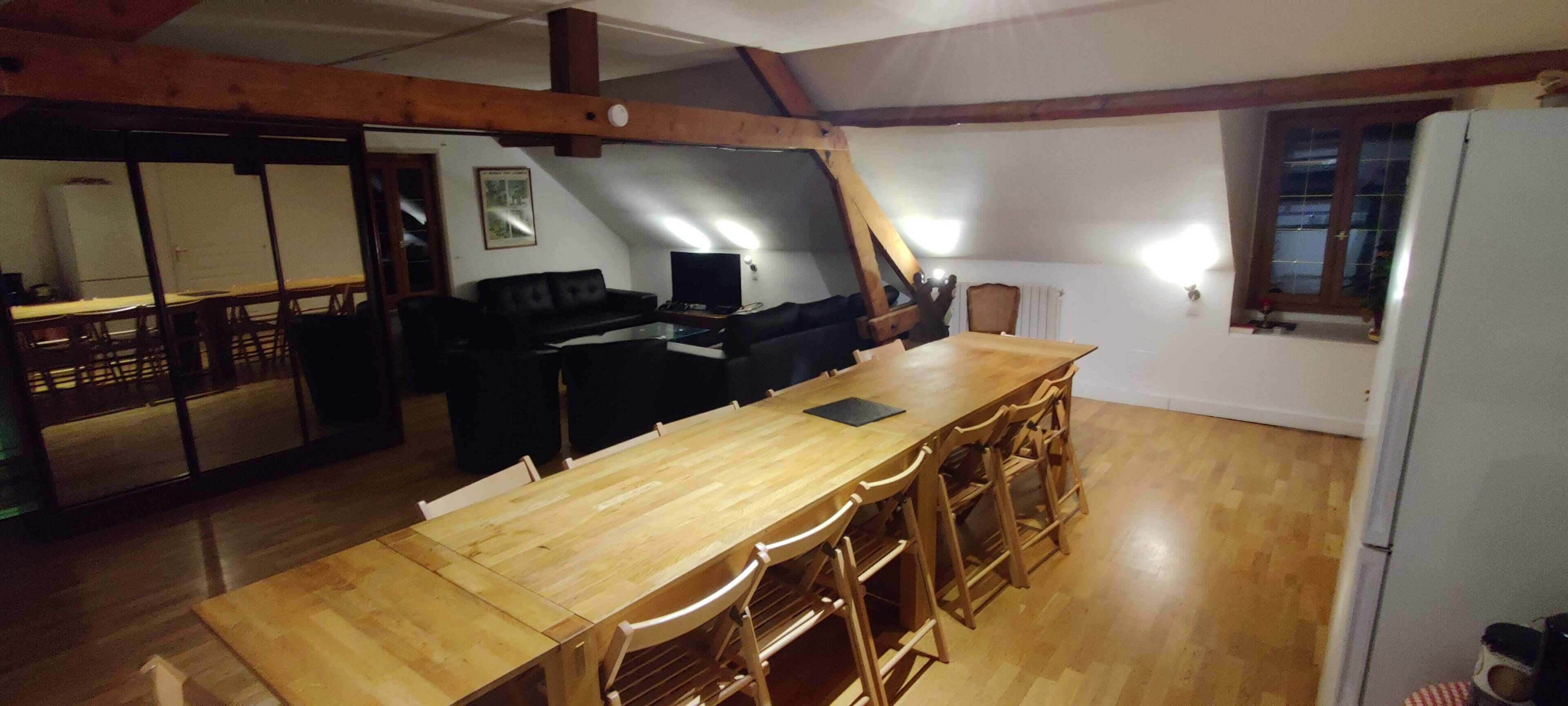 A dining area with a wooden table and chairs, a black sofa, and a television.