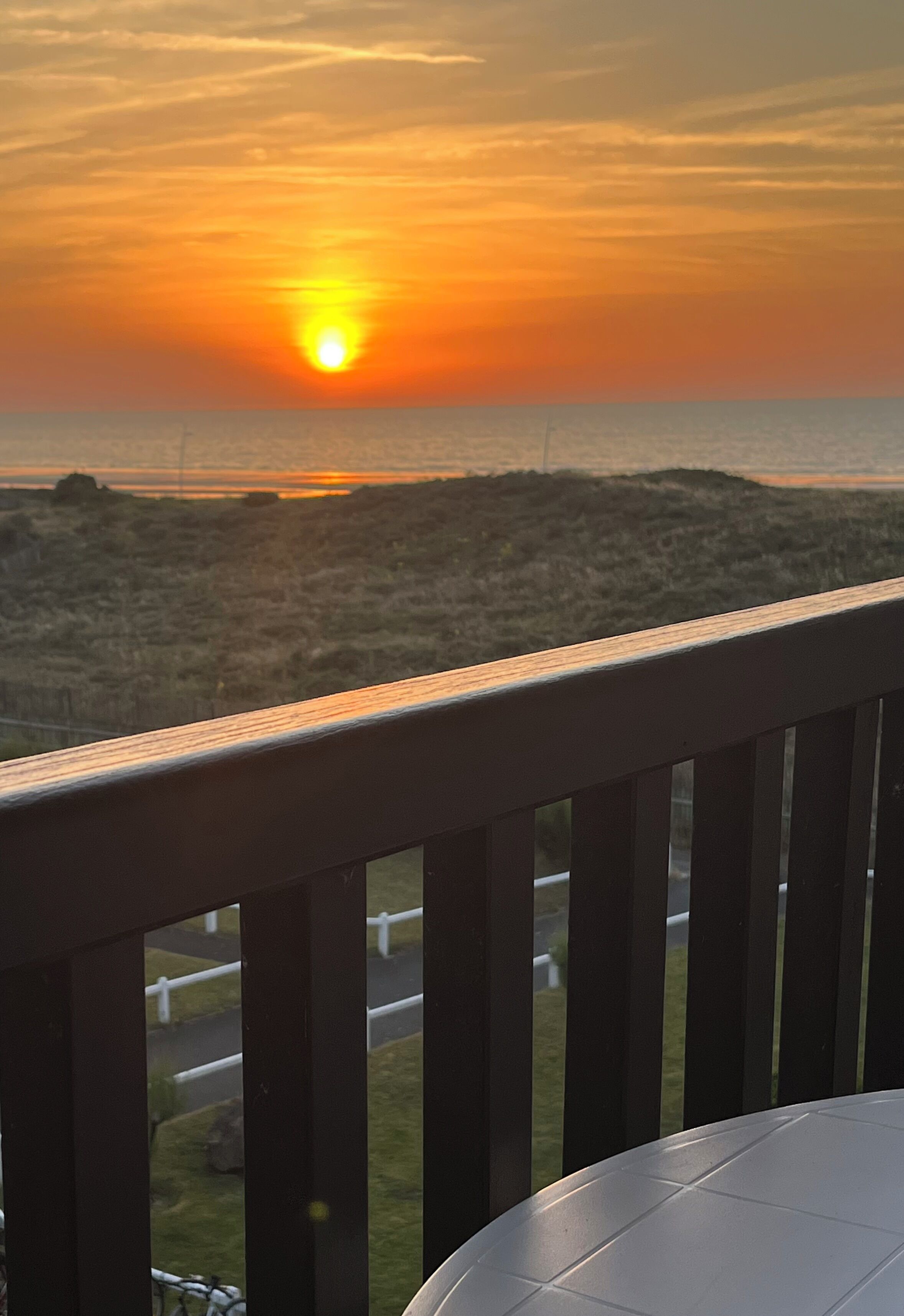 A sunset view from a balcony with a wooden railing.