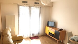 A living room with a sofa, a TV on a cabinet, a lamp, and a dining area with a table and chairs.