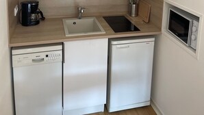 A compact kitchen with white cabinets, a dishwasher, a coffee maker, a sink, and a microwave.