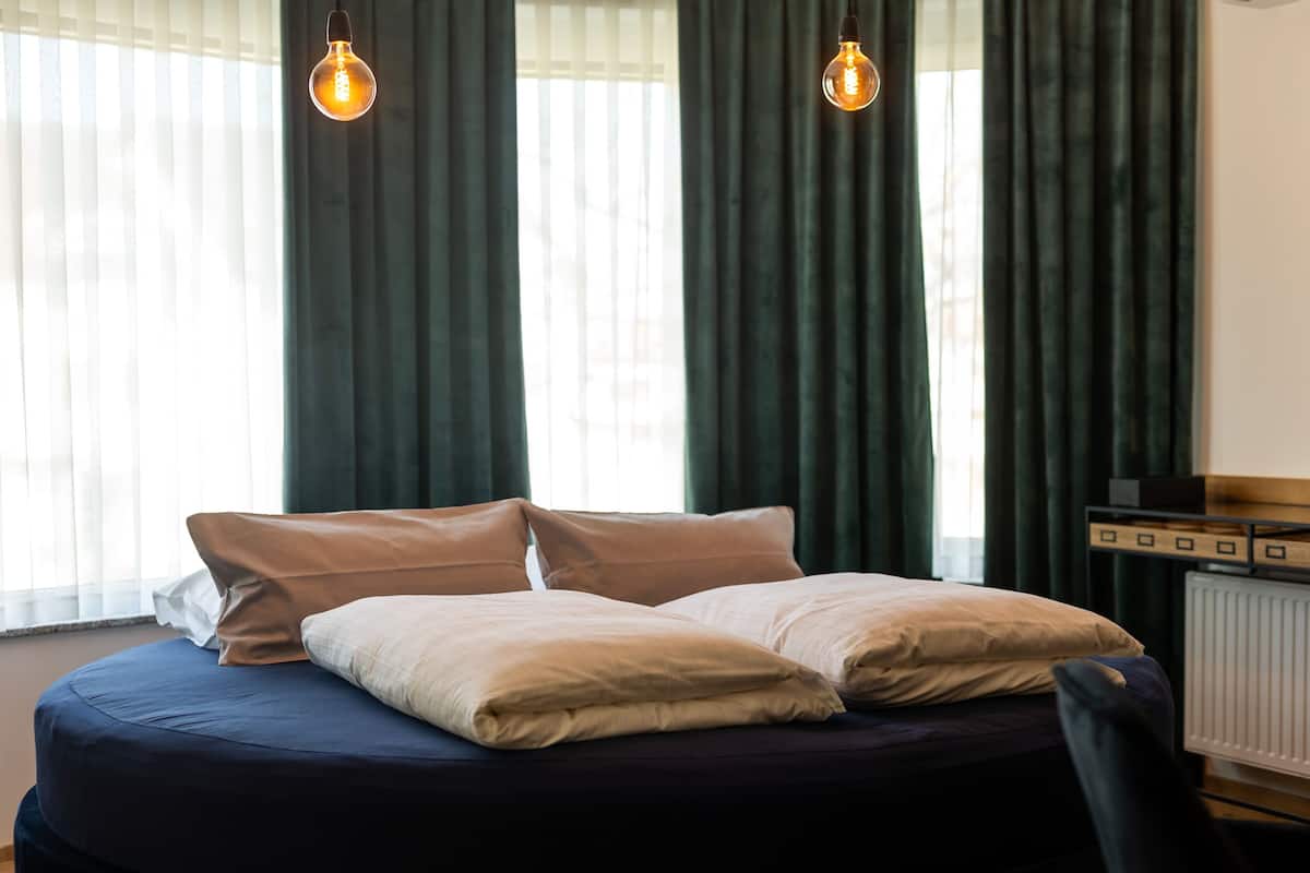 A neatly made bed with two pillows, a dark blue bedspread, and two hanging light bulbs.