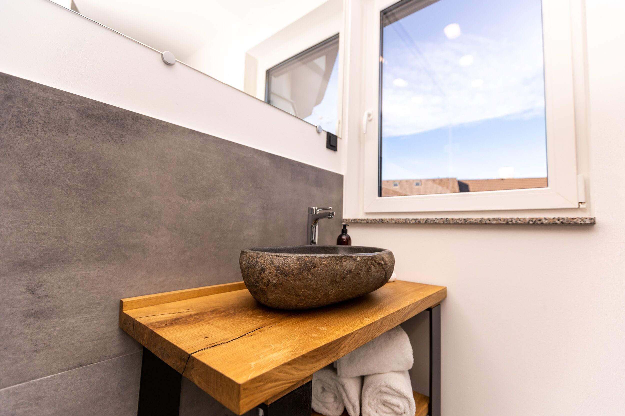 Een badkamer met een houten wastafelmeubel, een stenen wastafel en een raam boven de wastafel.