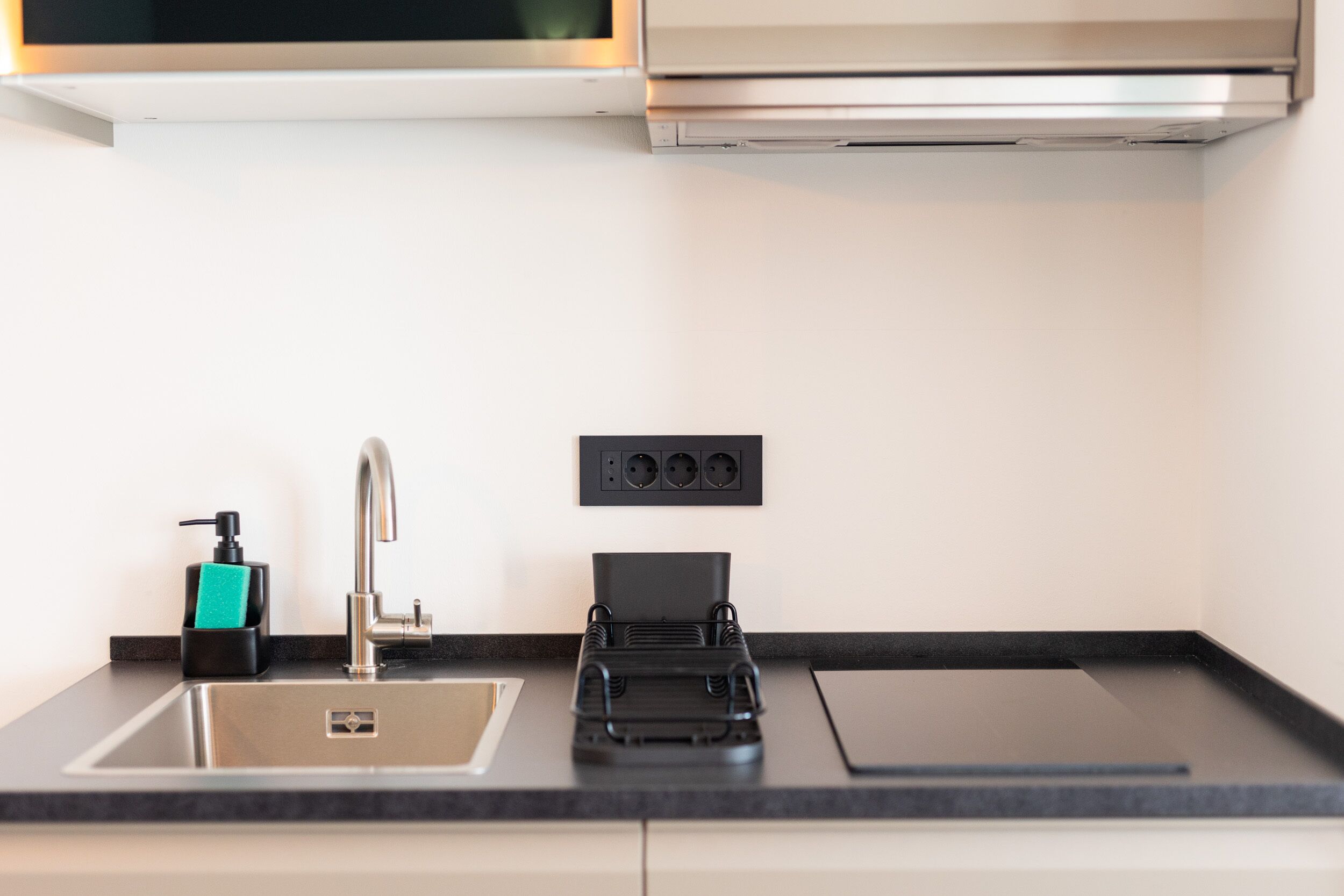 A modern kitchen with a stainless steel sink, a black soap dispenser, and a black appliance on the counter.