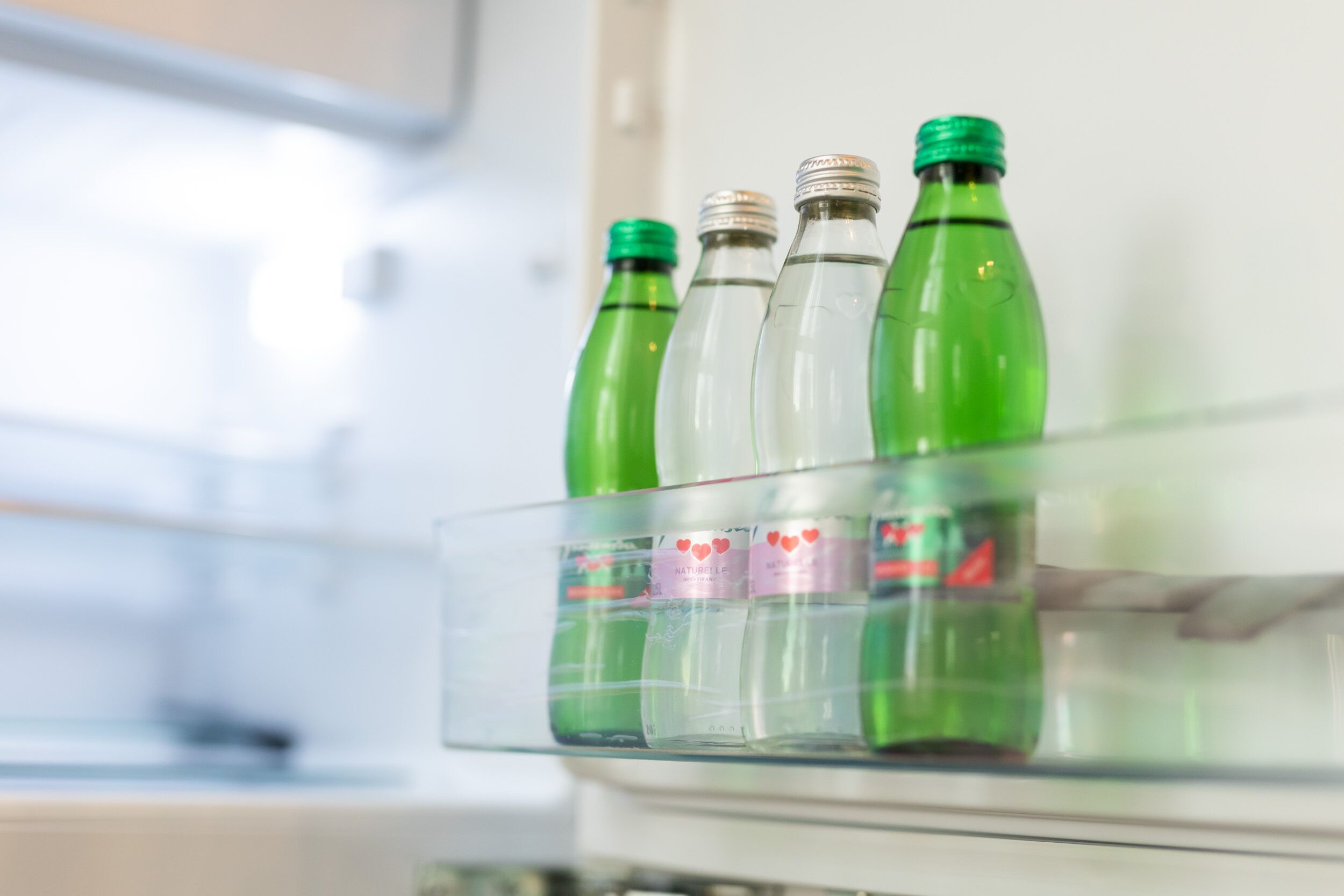 A refrigerator with a glass shelf holding several green bottles.
