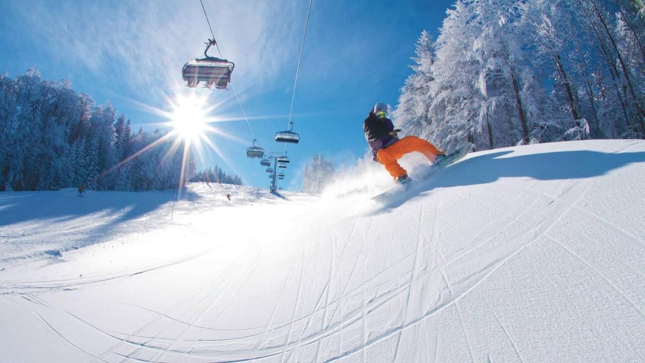 A ski slope with a person skiing, a ski lift, and snow-covered trees.