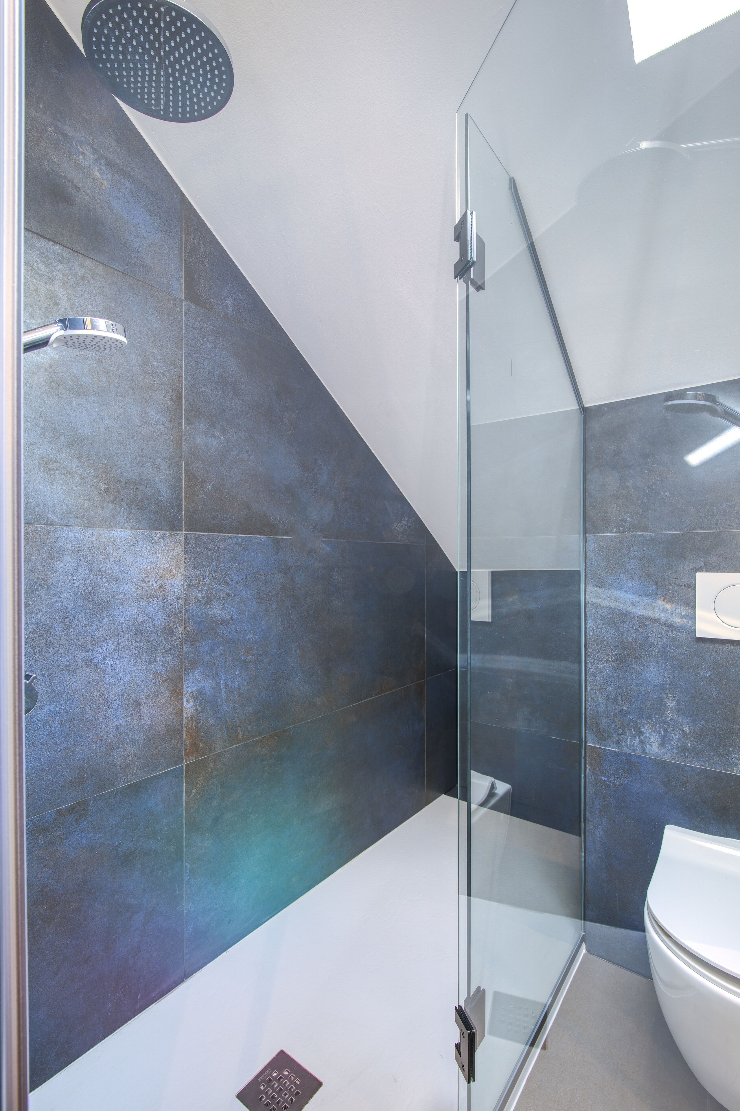 A modern bathroom with a glass shower enclosure, a white toilet, and a large mirror.