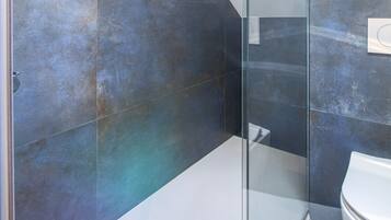 A modern bathroom with a glass shower enclosure, a white toilet, and a large mirror.