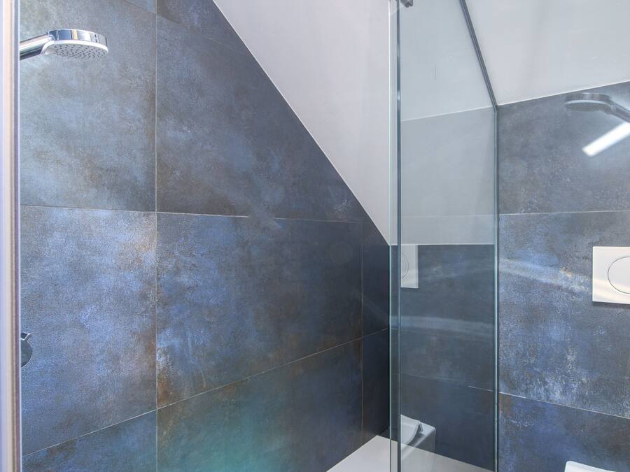 A modern bathroom with a glass shower enclosure, a white toilet, and a large mirror.