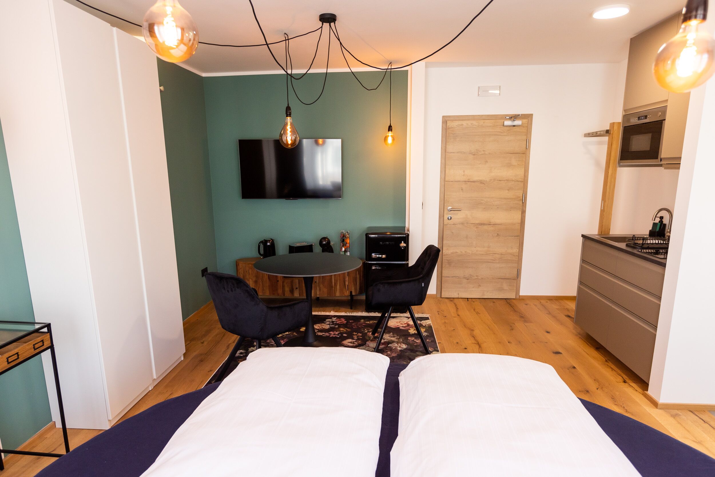 A modern room with a bed, a dining table, and a kitchen area.