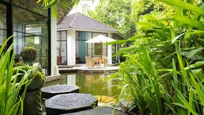 A serene garden with a pond, a seating area with a table and chairs, and a building with large windows. - Thalassa Dive & Wellbeing Resort Manado (Manado)