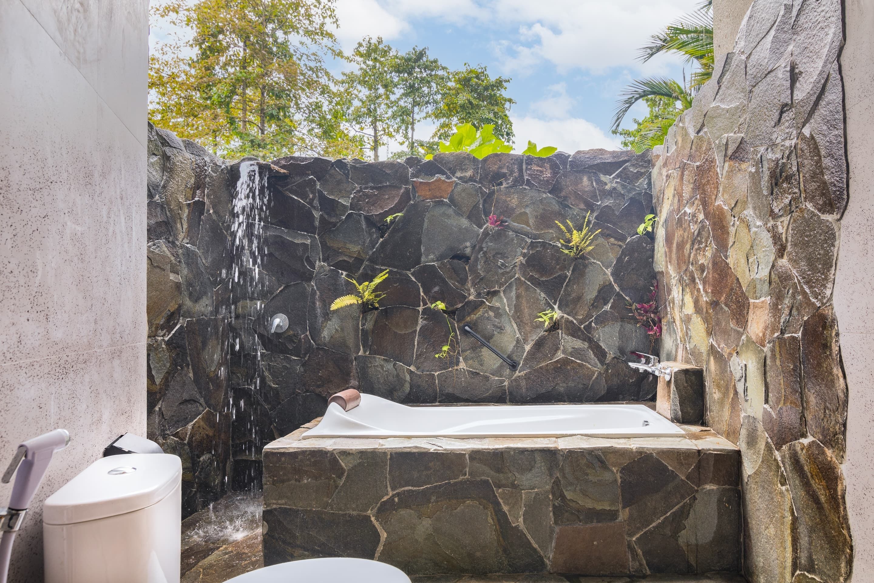 Un baño con paredes de piedra, una bañera empotrada, ducha y retrete.