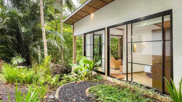 A modern house with large glass doors, surrounded by lush greenery and a garden path. - Thalassa Dive & Wellbeing Resort Manado (Manado)
