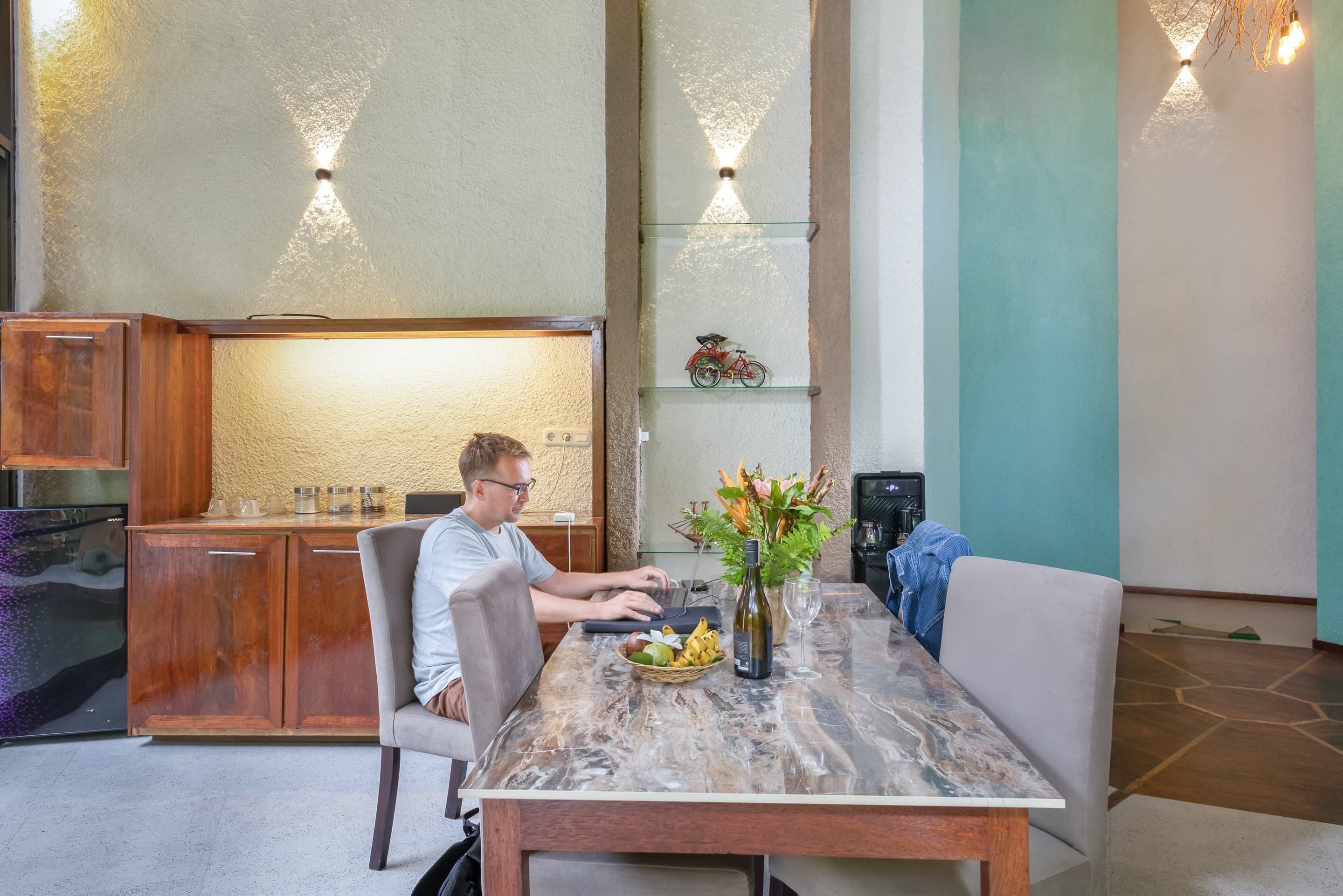 A dining area with a marble table, wooden cabinets, and a kitchen in the background.