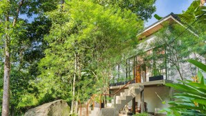 A modern house with a stone staircase leading to a wooden deck, surrounded by lush greenery and large rocks. - Thalassa Dive & Wellbeing Resort Manado (Manado)
