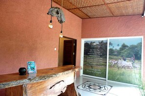 Una recepción con mostrador de madera, una lámpara colgante y un cartel que enumera servicios como spa, piscina y yoga.