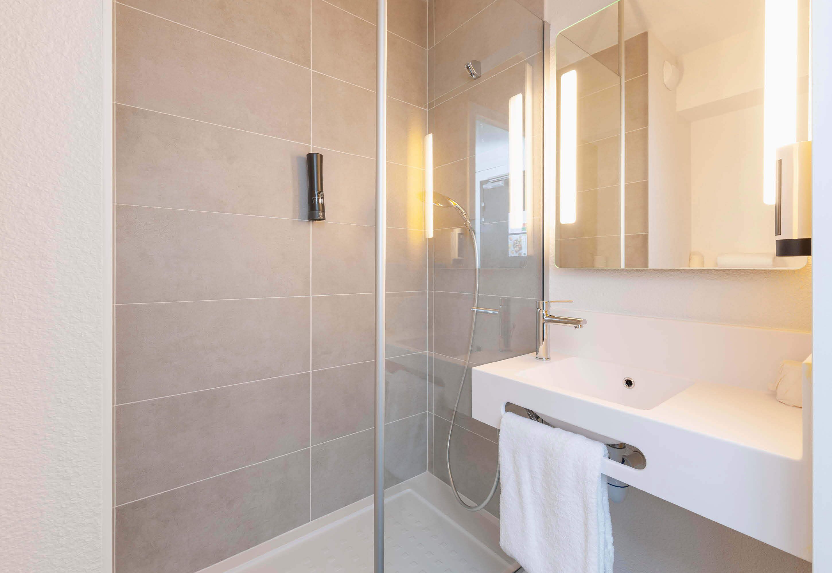 A modern bathroom with a glass-enclosed shower, a white sink, and a mirror above it.