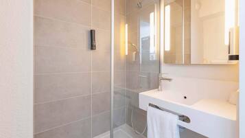 A modern bathroom with a glass-enclosed shower, a white sink, and a mirror above it.