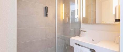 A modern bathroom with a glass-enclosed shower, a white sink, and a mirror above it.
