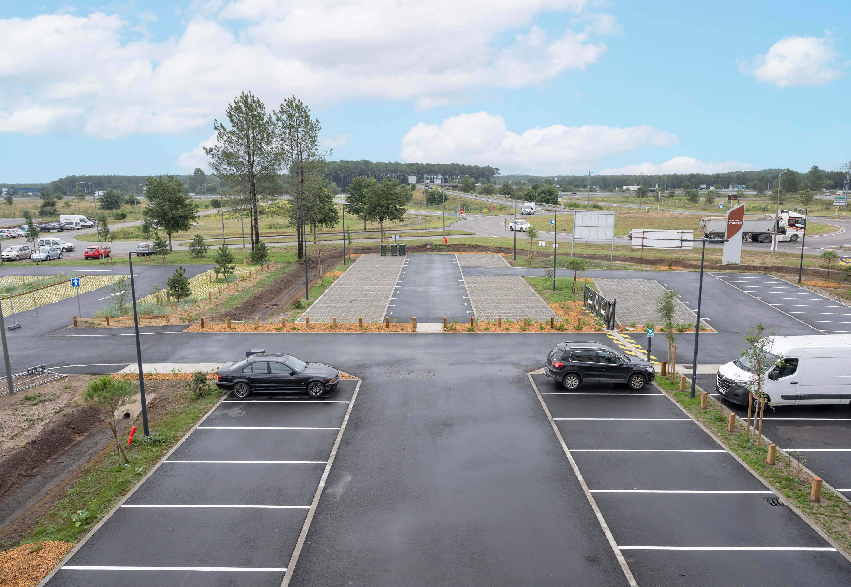 A parking lot with multiple rows of parking spaces, a road intersection, and a few vehicles.