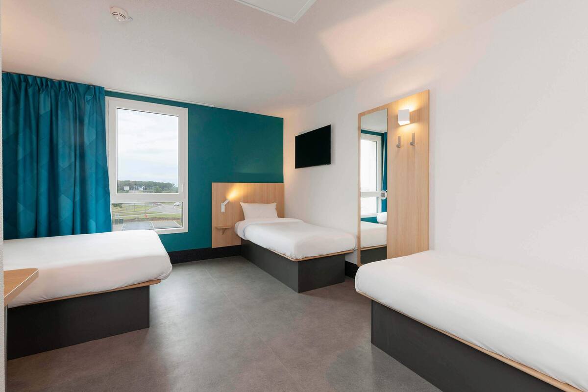 Quarto de hotel com duas camas de solteiro, uma janela grande, uma TV de tela plana e um espelho.