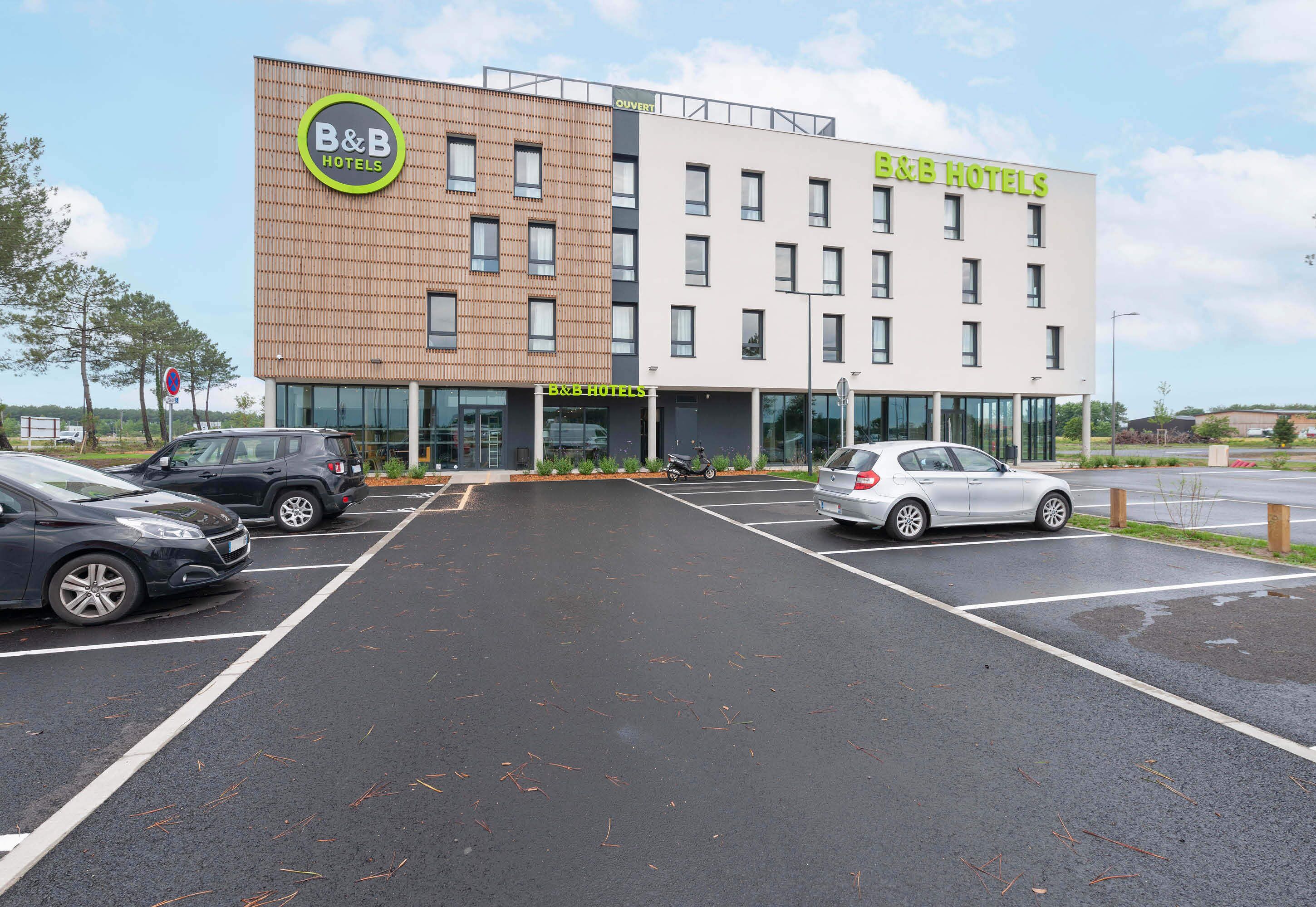 A B&B hotel with a modern design, featuring a mix of brick and white facades, and a parking lot with several cars.
