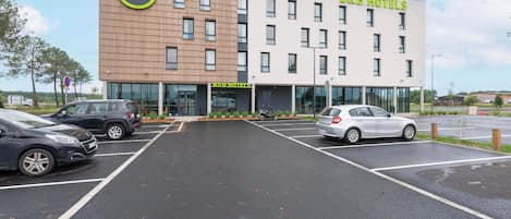 Un hôtel de type « bed and breakfast » au design moderne, avec une façade combinant des éléments en brique et des surfaces blanches, et un parking pouvant accueillir plusieurs voitures.