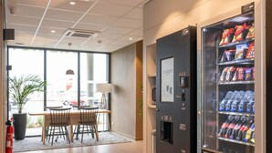 A hotel lobby with a vending machine stocked with snacks and beverages, a fire extinguisher, and a seating area with tables and chairs. - B&B HOTEL Saint-Geours-De-Maremne Hossegor (Saint-Geours-de-Maremne)