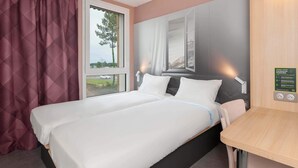 A hotel room with a bed, a window, a wall-mounted light, and a small table. - B&B HOTEL Saint-Geours-De-Maremne Hossegor (Saint-Geours-de-Maremne)