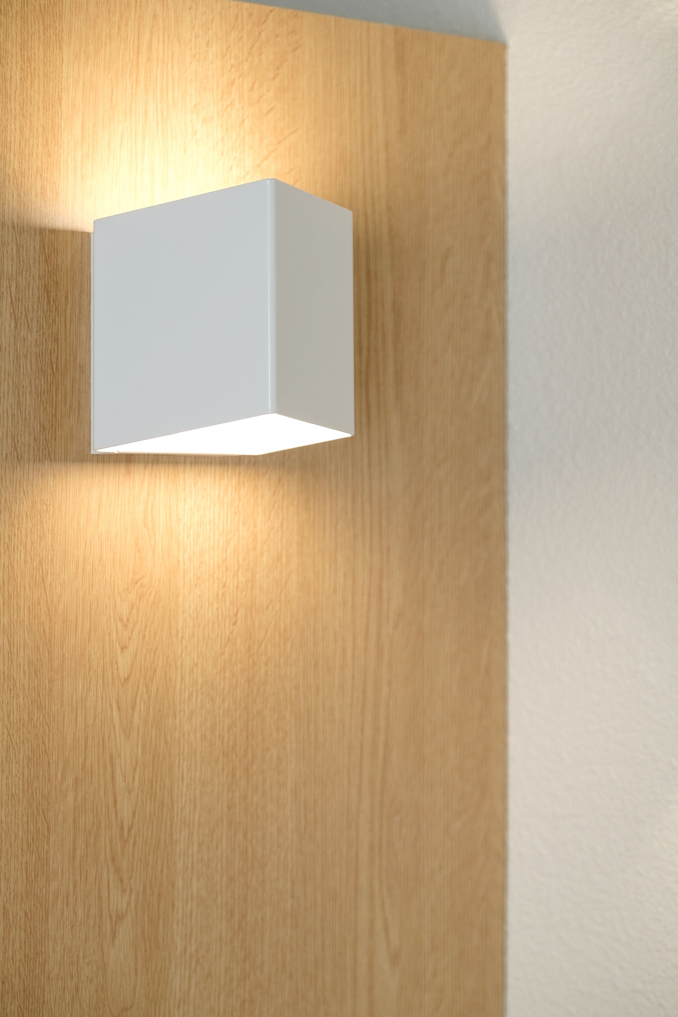 Een moderne wandlamp tegen een houten paneel en een witte muur.