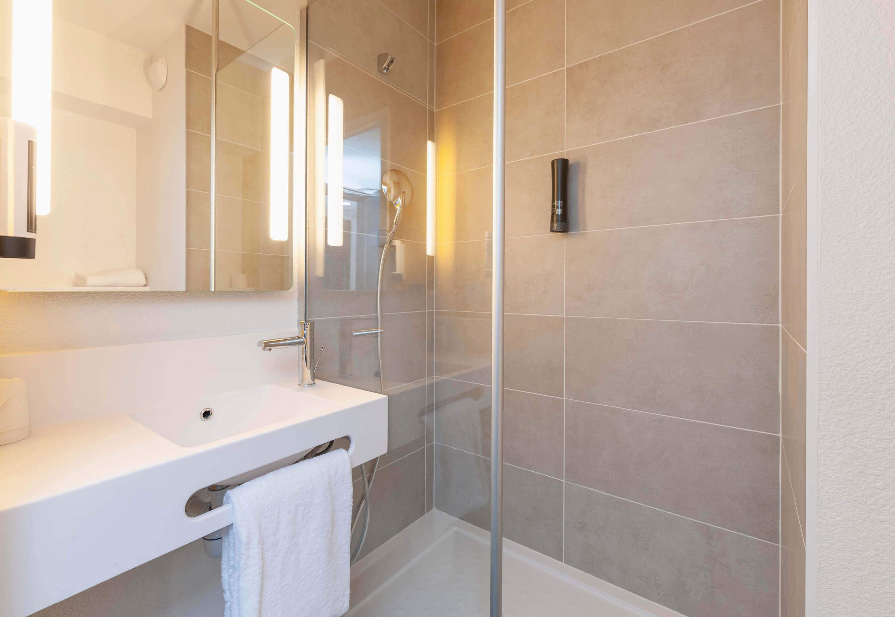 Un baño moderno con lavamanos blanco, espejo y ducha con mampara de vidrio.