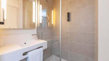Un baño moderno con lavamanos blanco, espejo y ducha con mampara de vidrio.