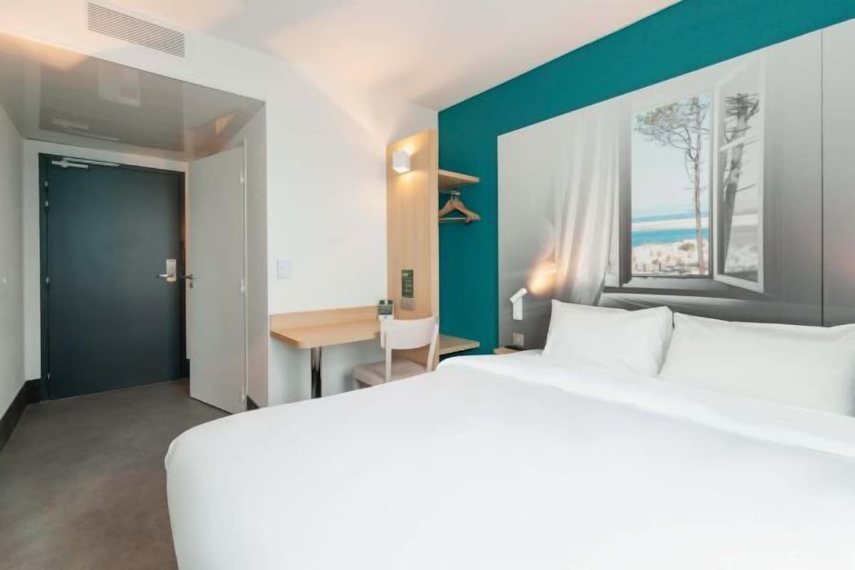 Ein Hotelzimmer mit Bett, Schreibtisch, Stuhl, Kleiderschrank, einem Fenster mit Blick auf den Strand und einer Tür.