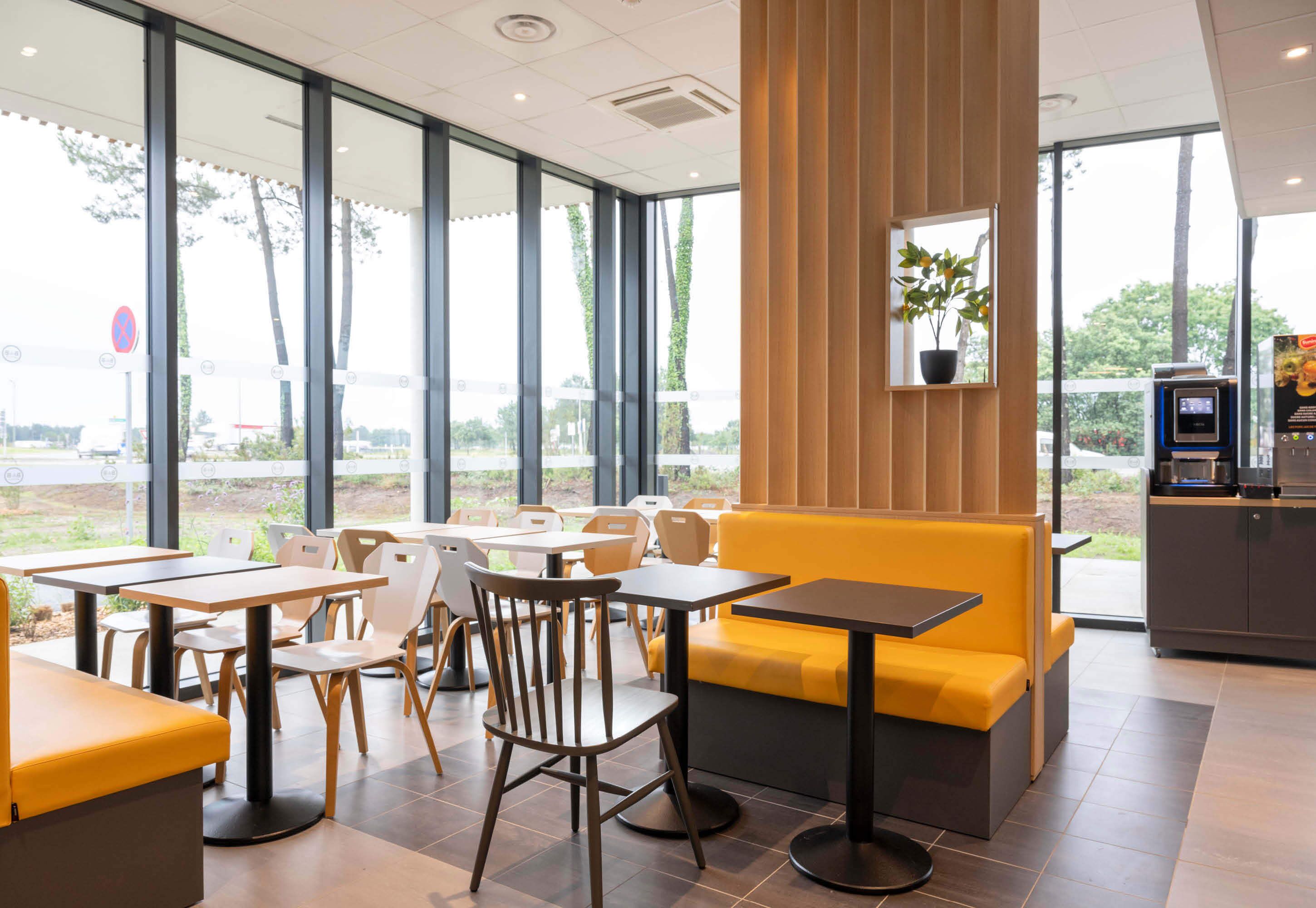 A modern cafe with yellow seating, large windows, and a vending machine.