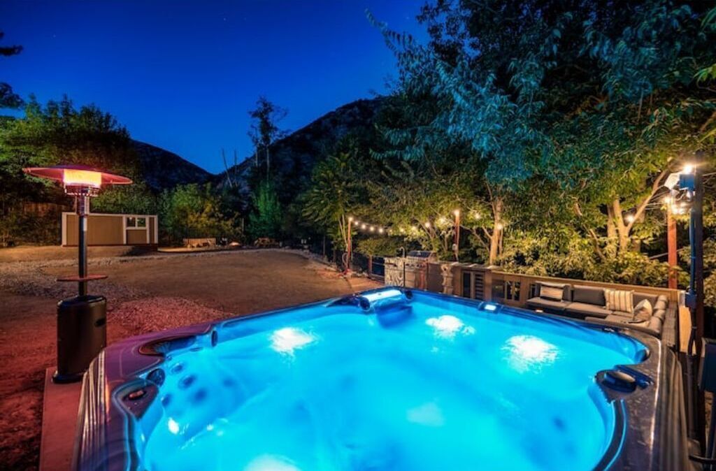 A hot tub with a blue light, surrounded by trees and a mountain in the background.