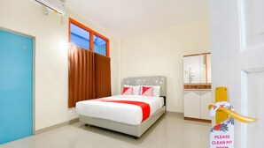 Une chambre d’hôtel avec un lit, une porte bleue, une fenêtre avec des rideaux, une table de chevet et un miroir.