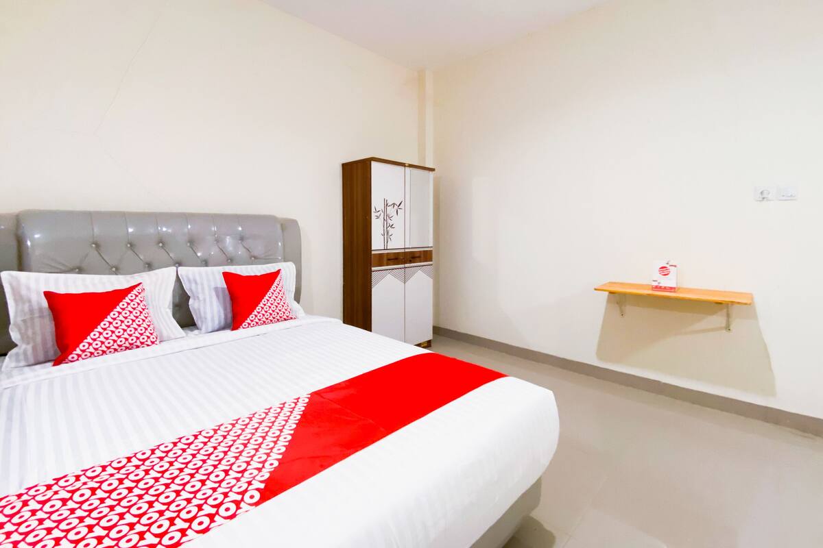 A neatly made bed with a red and white bedspread, a grey tufted headboard, and two red pillows.