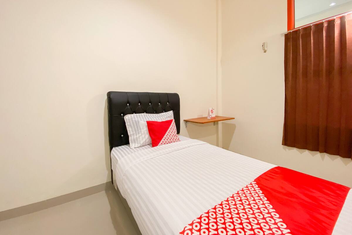 A neatly made bed with a striped white and red bedspread, a black upholstered headboard, and a small bedside table with a red object on it.