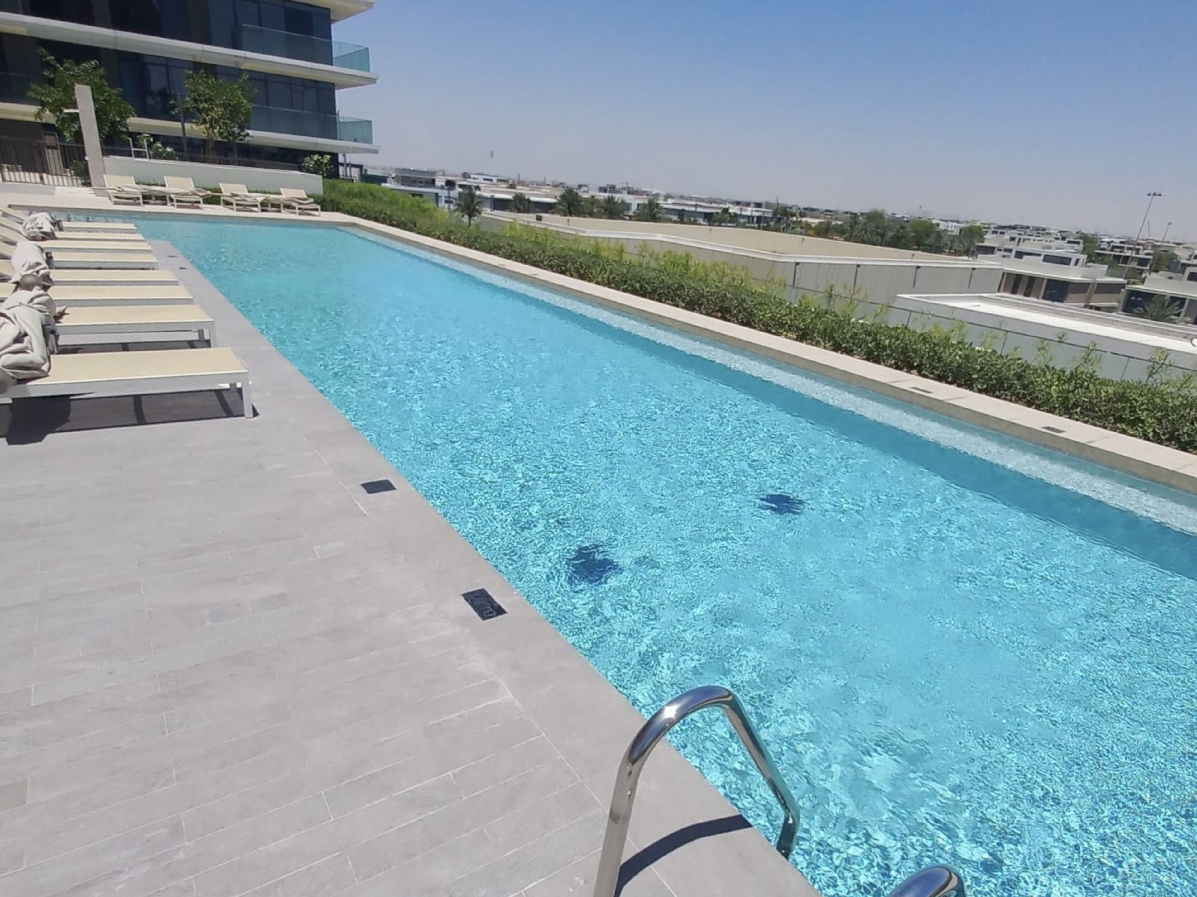 Une piscine avec des chaises longues et un bâtiment moderne en arrière-plan.