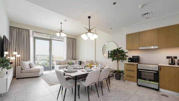 A modern kitchen with a built-in oven and a dining area with a table set for four. - Maison Privee - Graceful Apt in Prestigious Dubai Hills close to the Golf Course (Dubai)