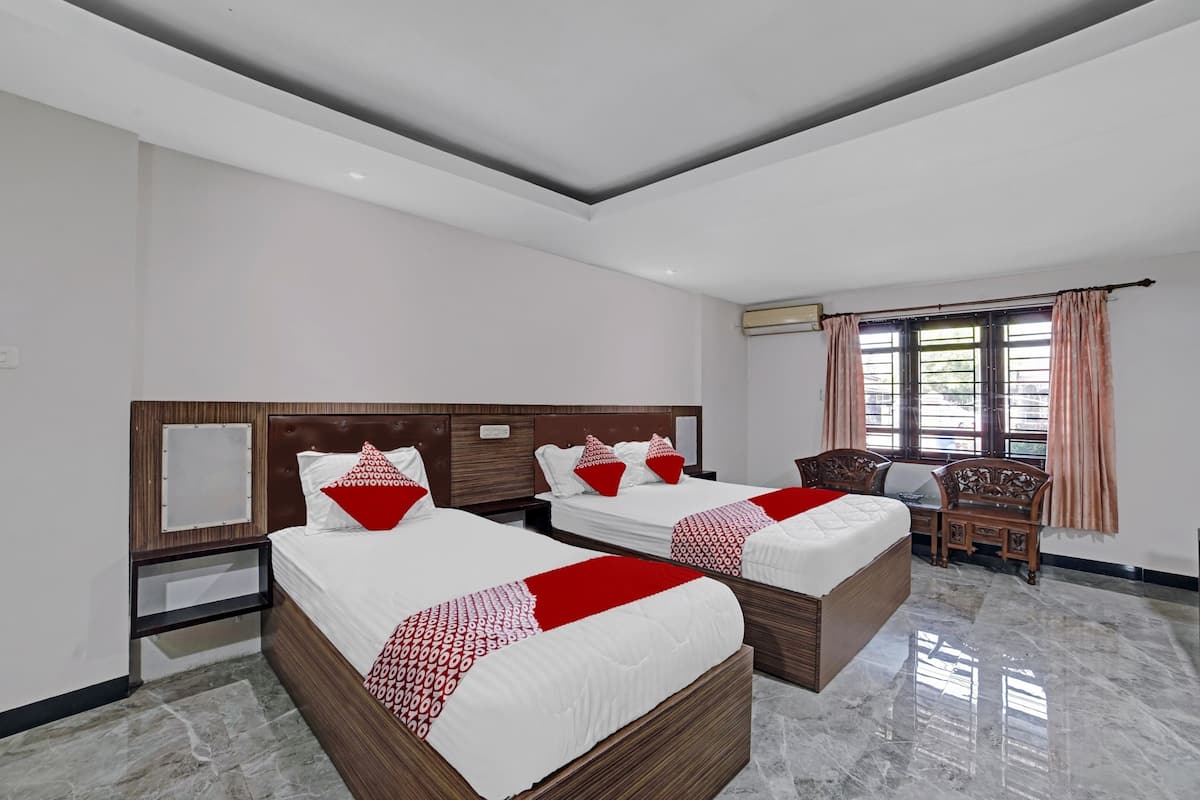 A hotel room with two beds, a wooden headboard, a small wooden table, and a window with curtains.