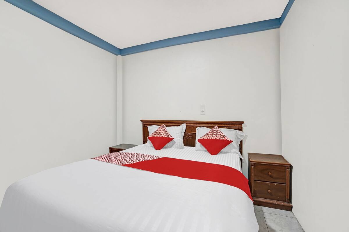 A bedroom with a bed, two nightstands, and a red and white patterned throw blanket.